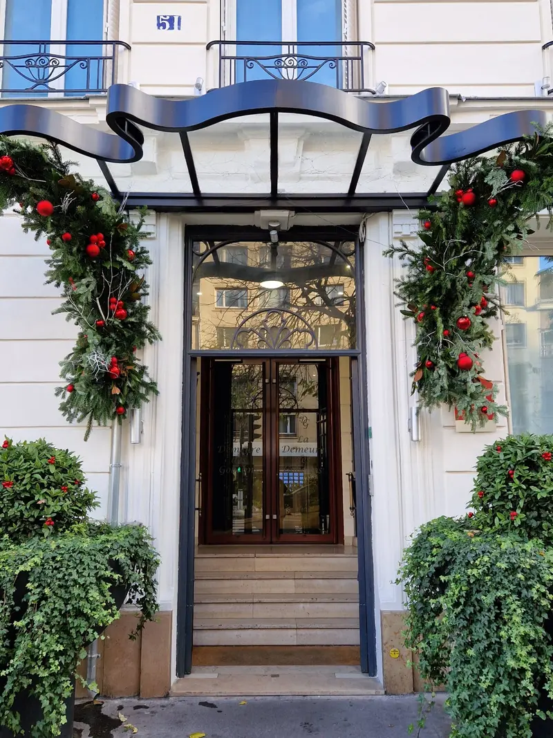 Porche d'un hôtel parisien habillé de sapin et de boules rouges, entre deux topiaires de lierre